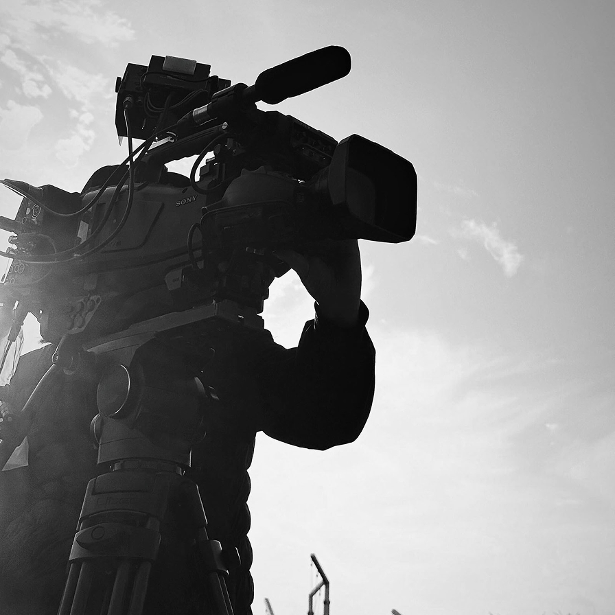 逆光の空を背景にカメラを構えるスタッフのシルエット(モノクロ写真)