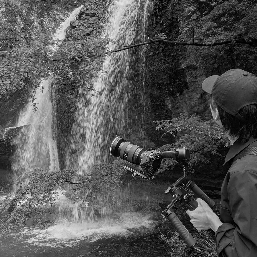 ジンバルカメラで滝を撮影するスタッフ(モノクロ写真)