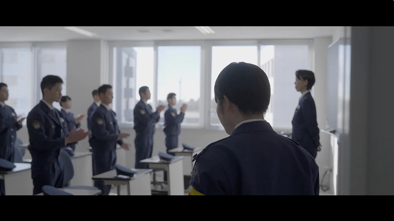 制服姿の人々が教室で拍手をする制作実績動画のワンシーン